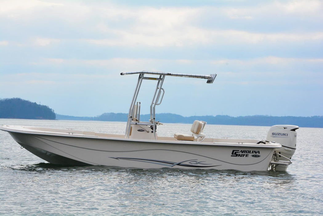 A Carolina Skiff 198 DLV boat with a beige hull and a chrome T-top, powered by a Suzuki outboard engine, cruising on calm water with mountains in the background.