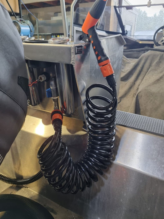 A portable marine washdown system with a coiled hose, spray nozzle, and quick-connect fittings, mounted on a boat deck.