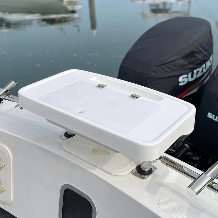 White, rectangular fishing bait station mounted on the back of a boat with two outboard motors covered in black engine covers. The station has a hinged lid and several smaller compartments. The "SUZUKI" logo is visible on one of the engine covers.