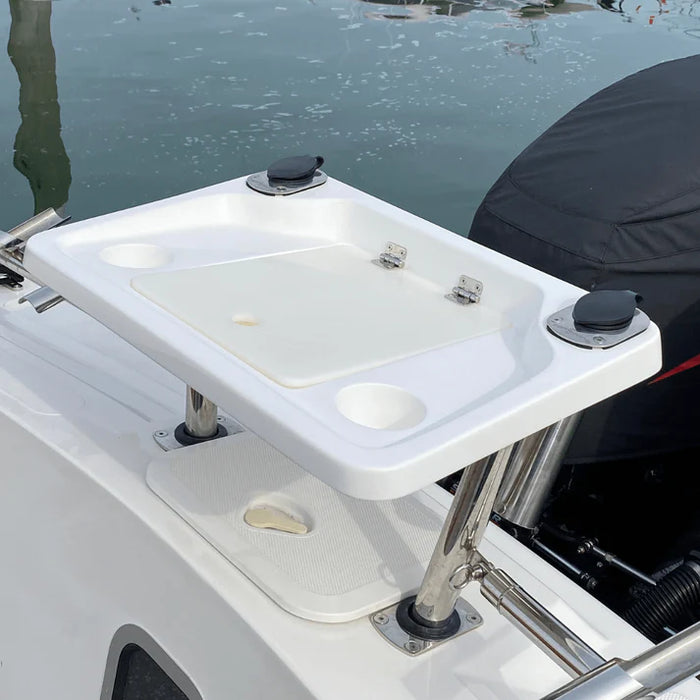 A white, rectangular fishing bait station mounted on the back of a boat with two outboard motors covered in black engine covers. The station has a hinged lid that is partially open, revealing a large, rectangular compartment with several smaller compartments around it. The "SUZUKI" logo is visible on one of the engine covers. There are two rod holders on the back of the station.